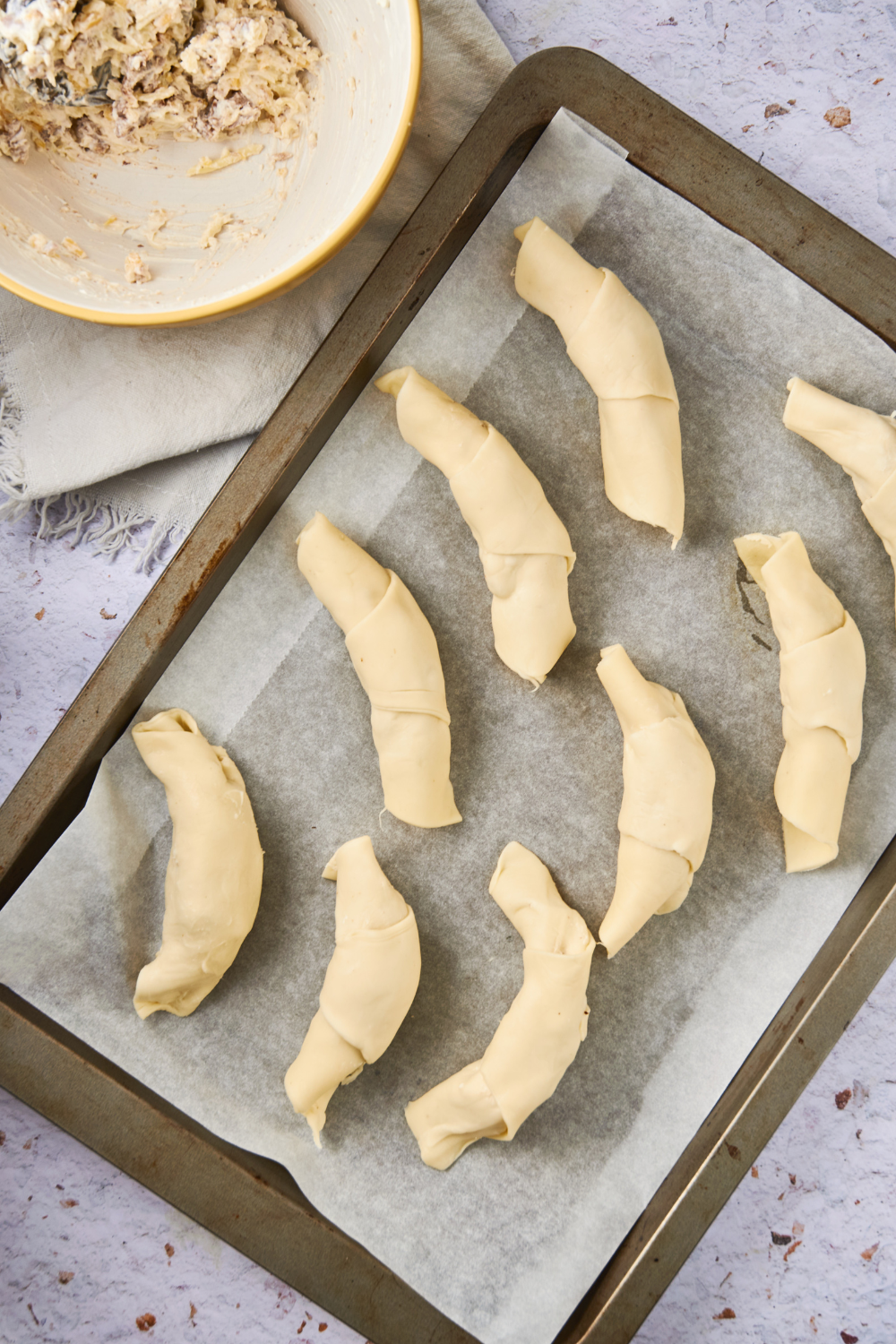 A bunch of crescent rolls with a sausage cream cheese filling on a baking sheet lined with parchment paper.