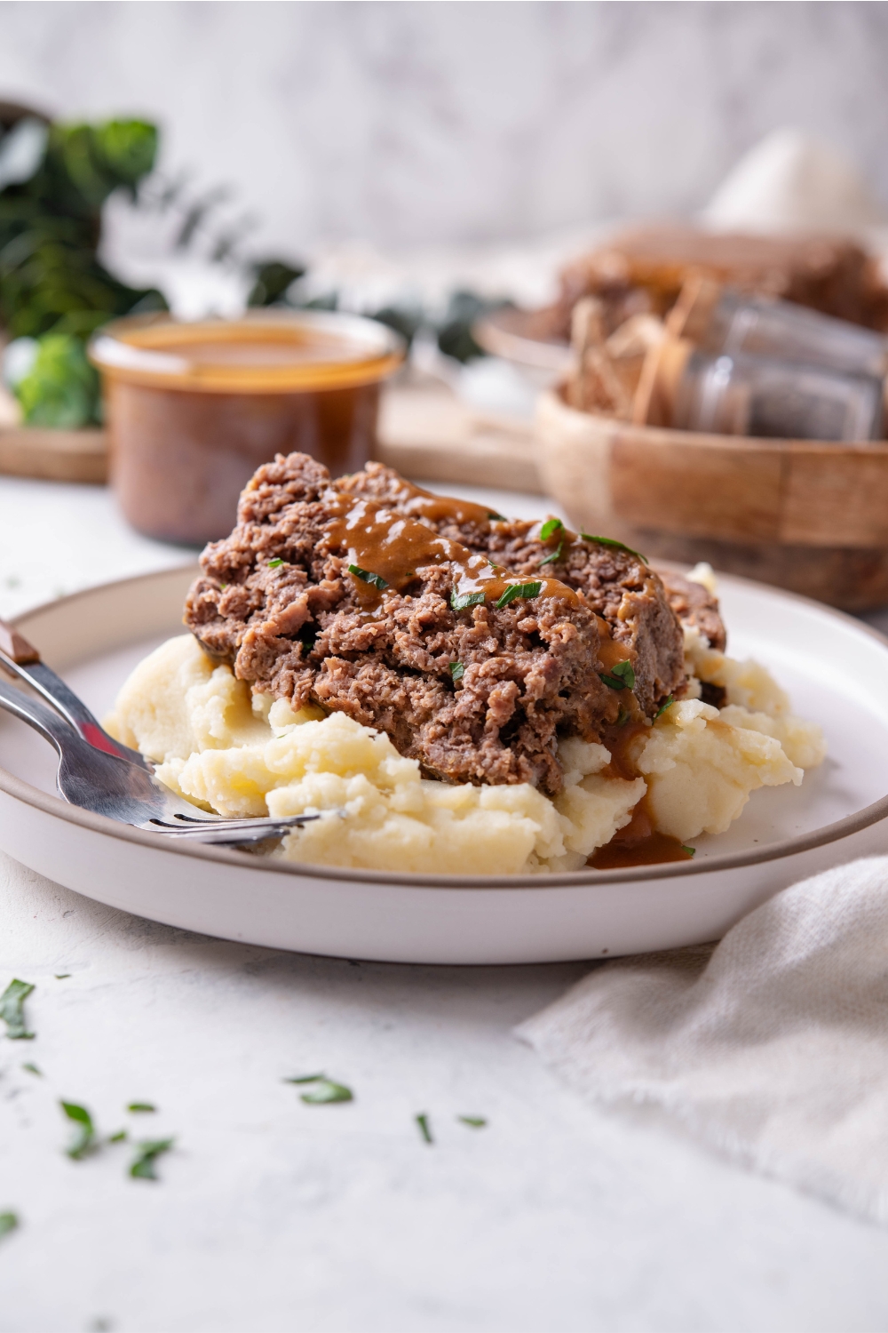 A plate with meatloaf served on mashed potatoes topped with brown gravy. Two forks sit next to the food.