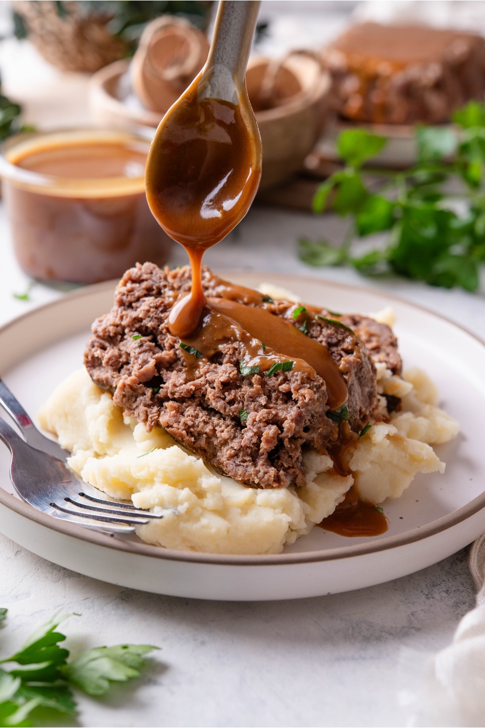 A plate with meatloaf served on mashed potatoes being topped with brown gravy.