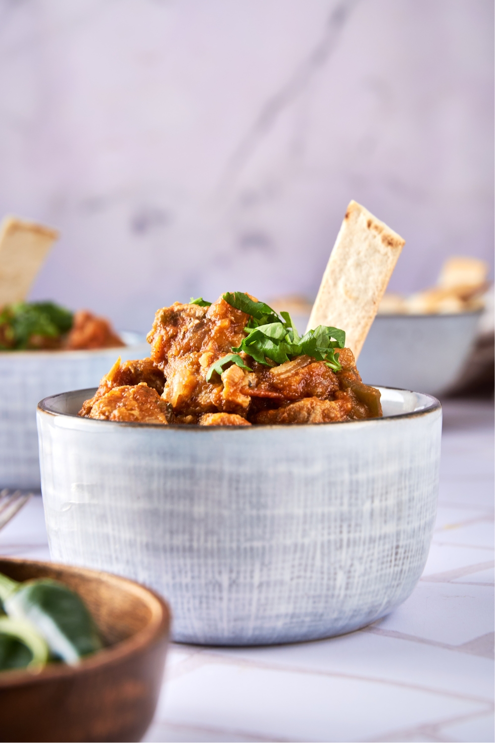 A heaping bowl full of pork green chili garnished with a pita bread slice.