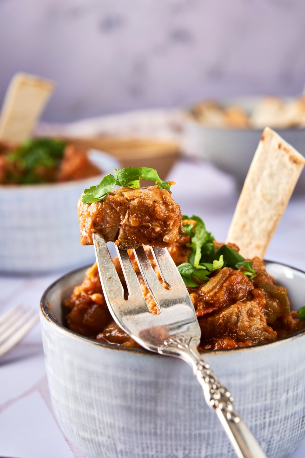 A fork with a piece of pork green chili with a bowl full in the background.