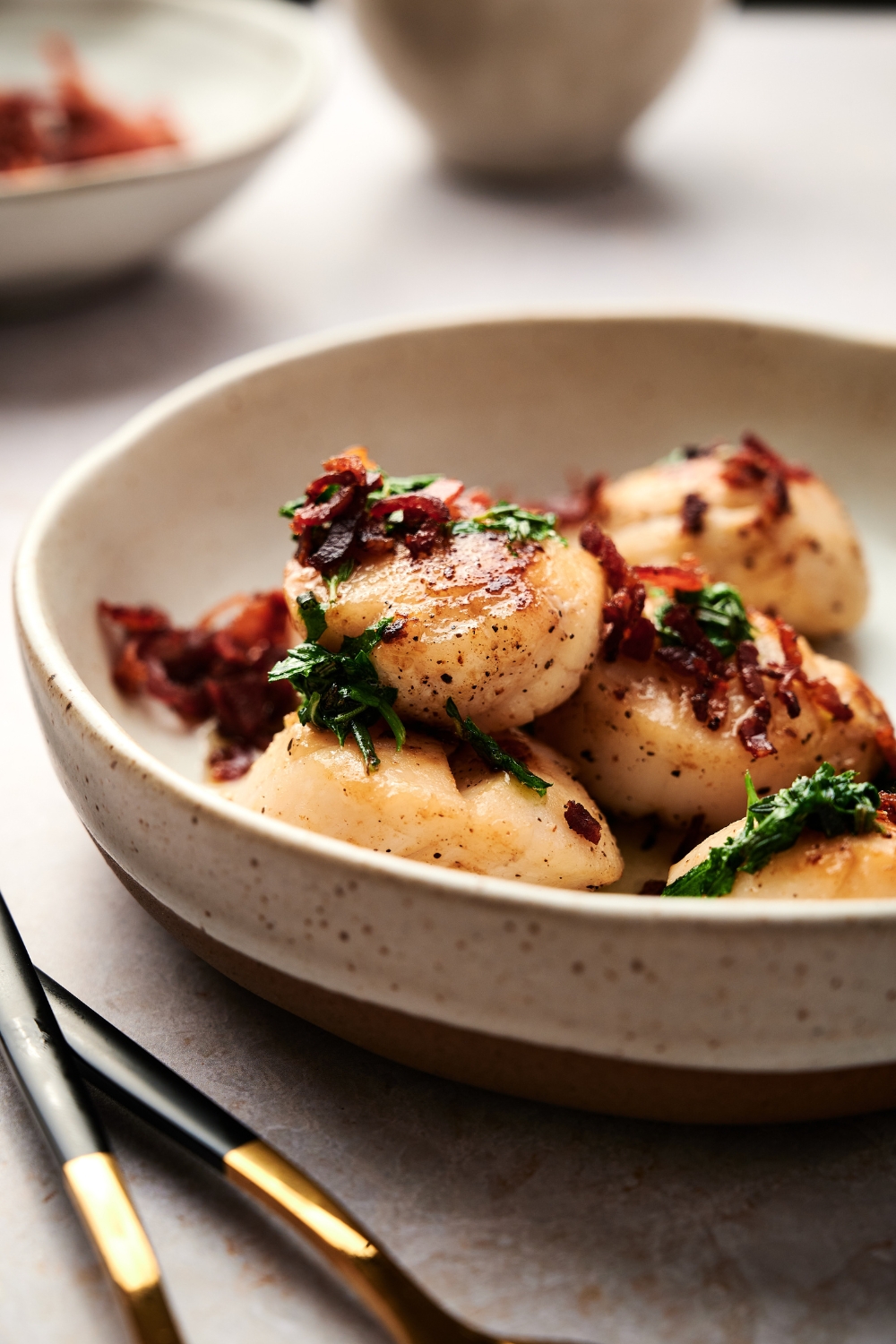 A bowl with cooked scallops topped with parsley and crispy bacon.