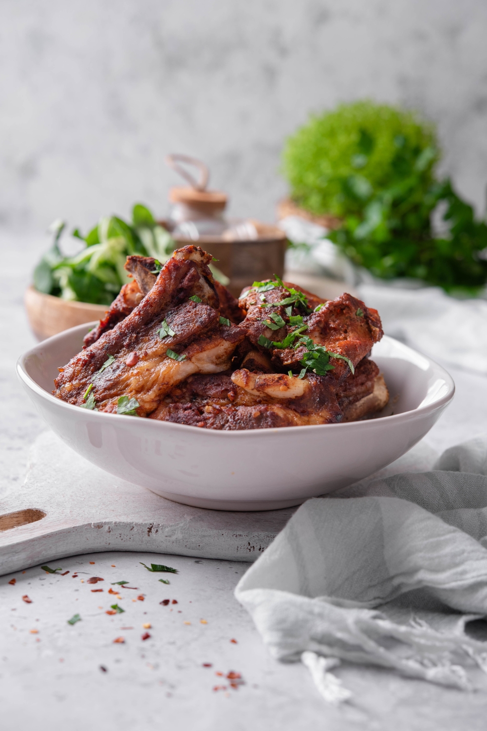 A white bowl is full of country style ribs. The ribs are perfectly cooked and garnished with fresh parsley.
