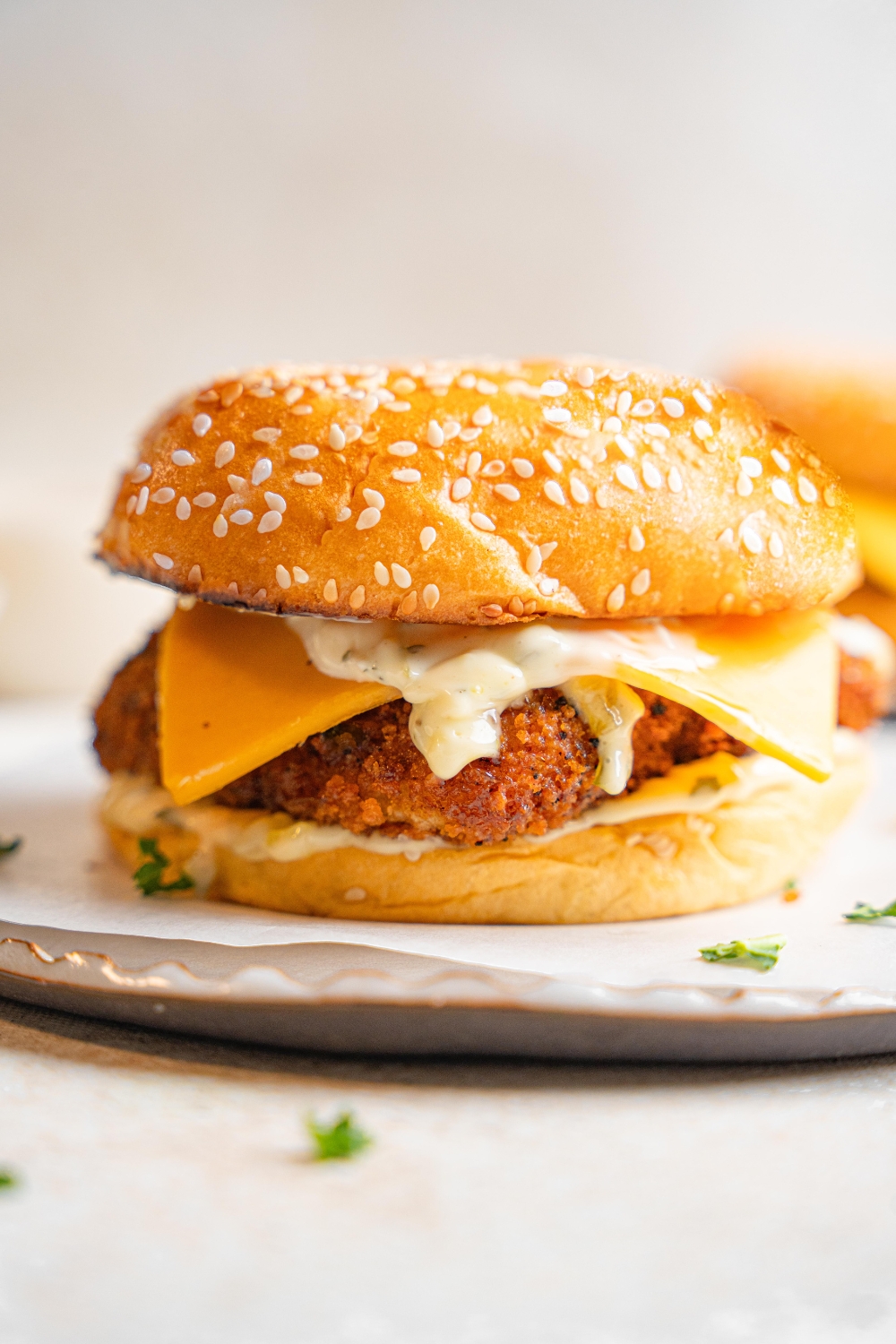 A filet o fish sandwich sits on a white plate. Garlic aioli and cheddar cheese can be seen between the buns.