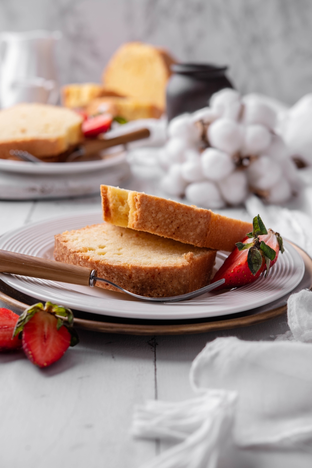 A white plate holds two slices of old fashioned pound cake. A fork rests on the plate.