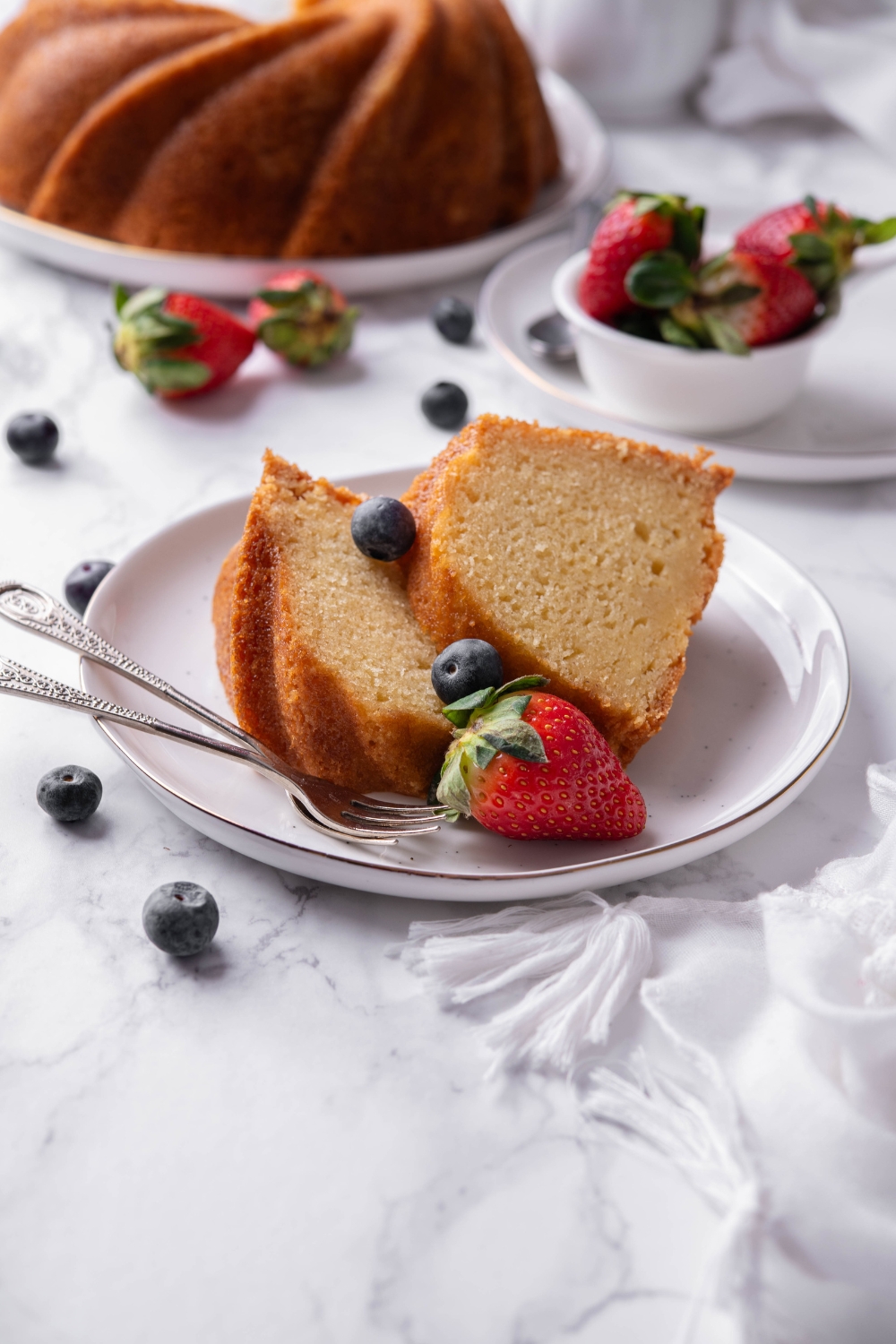 Two large slices of buttermilk pound cake are on a white plate. Fresh berries garnish the plate.