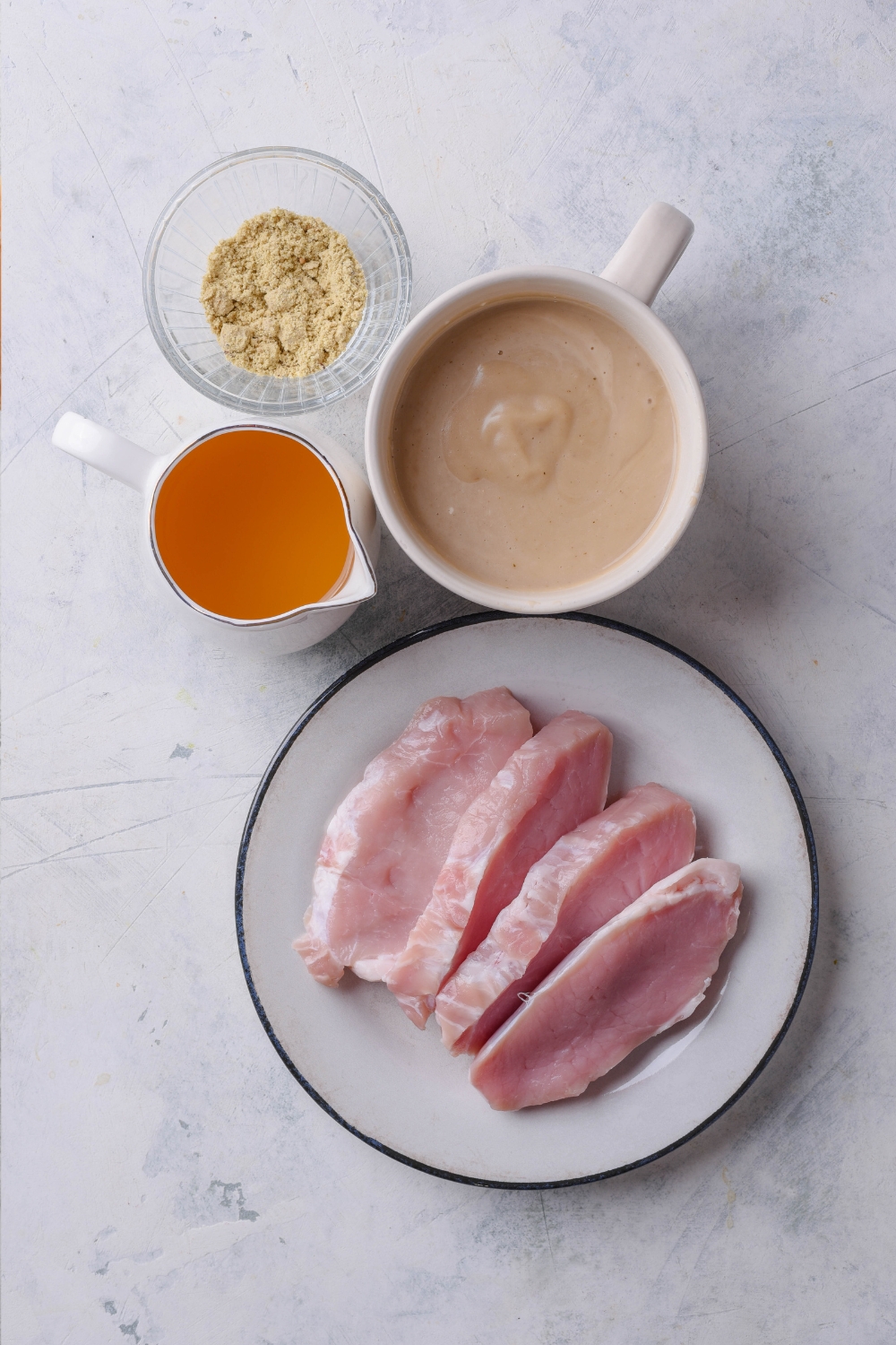 Onion soup mix, mushroom soup, chicken stock, and pork chops are all in separate dishes on a gray counter.