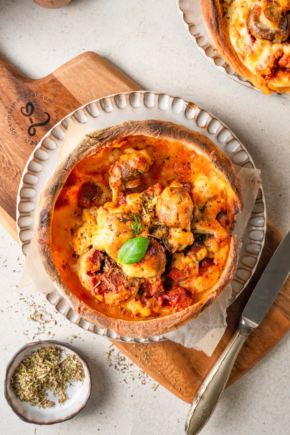 A baked Chicago pizza pot pie sits on a white plate. It is garnished with a basil leaf.