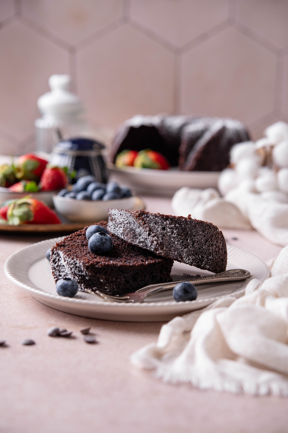 Two thick slices of chocolate pound cake are sitting on a white plate. There are fresh blueberries on the cake and a fork resting on the plate.