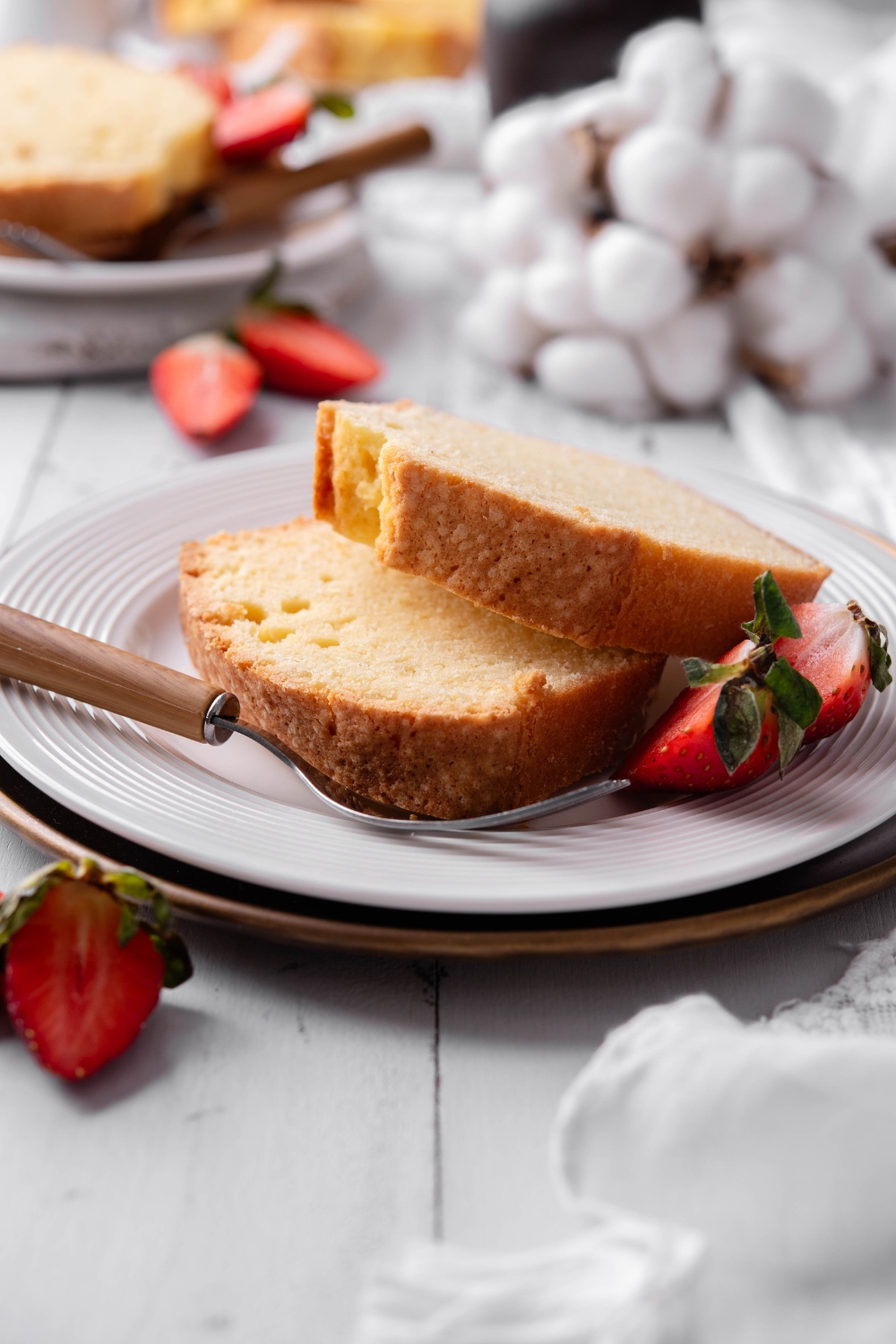 Two slices of old fashioned pound cake rest on a white plate. The plate is garnished with strawberries.