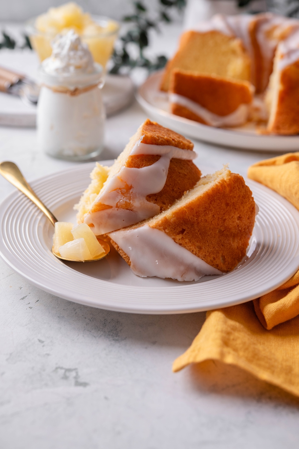 Two slices of pineapple pound cake sit on a white plate. A fork holds pieces of pineapple.