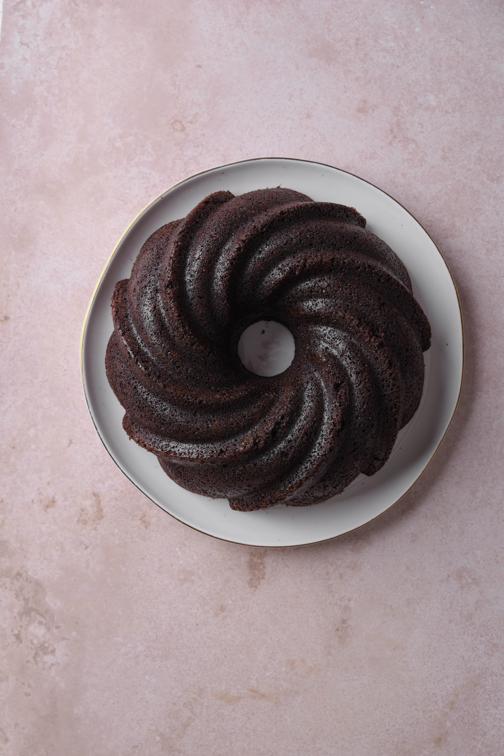 A baked and cooled chocolate pound cake is sitting on a white serving plate.
