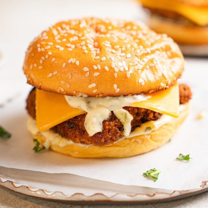A filet o fish sandwich sits on a white plate. Garlic aioli and cheddar cheese spill from the buns.