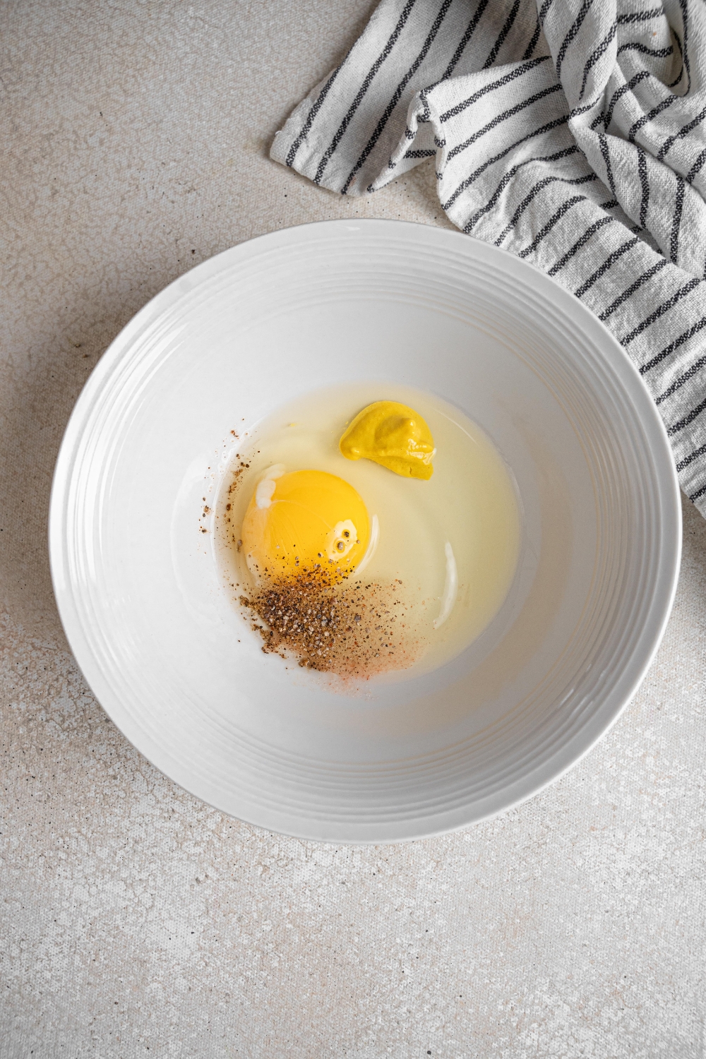 A white mixing bowl holds an egg, mustard, and seasonings.