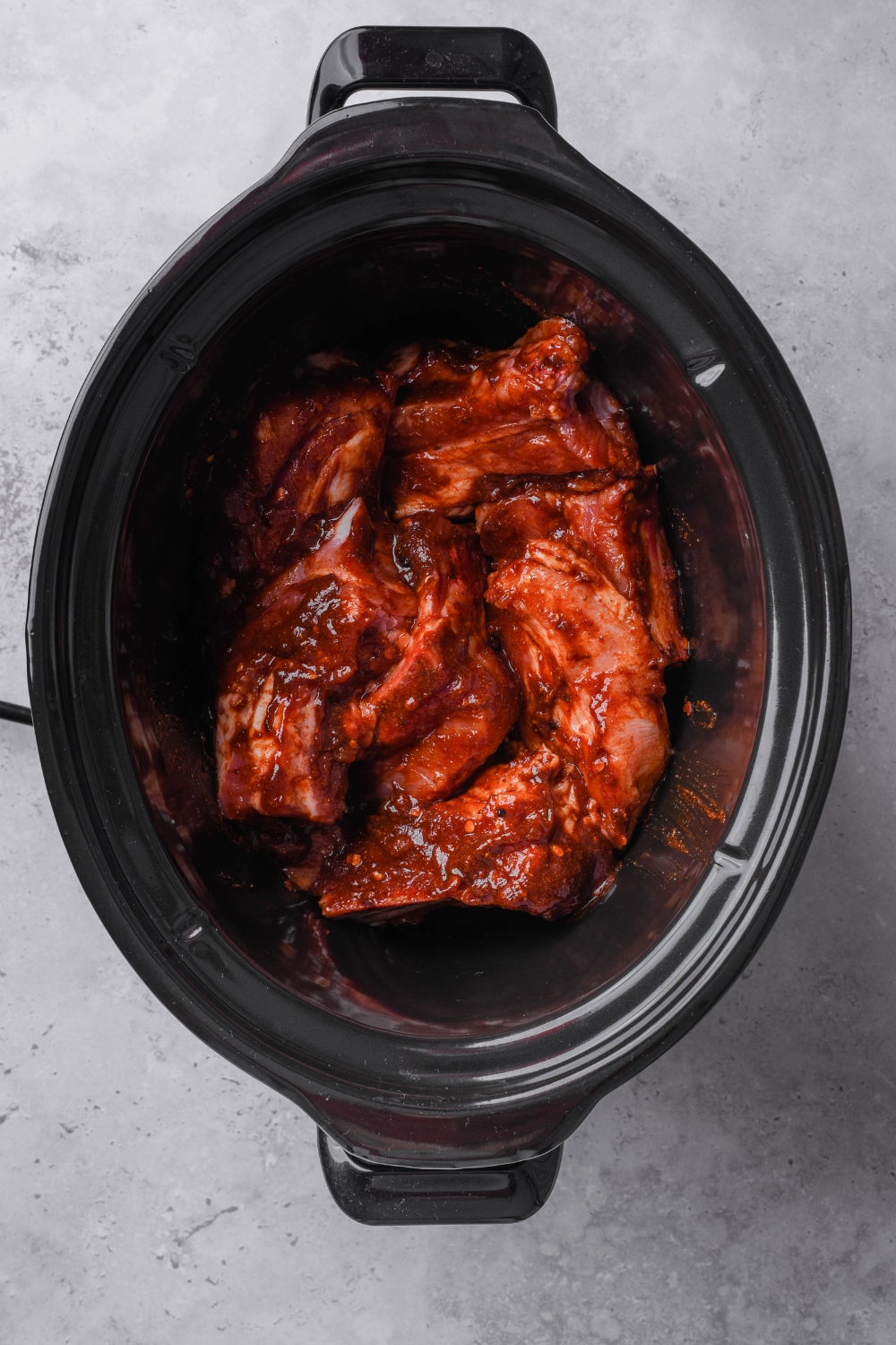 A black crock pot is full of barbecue country style ribs covered in sauce.