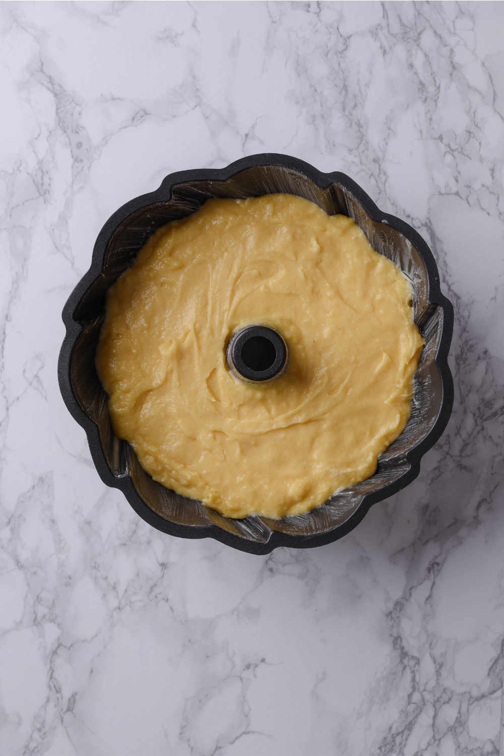 A black bundt pan holds buttermilk pound cake batter waiting to be baked.