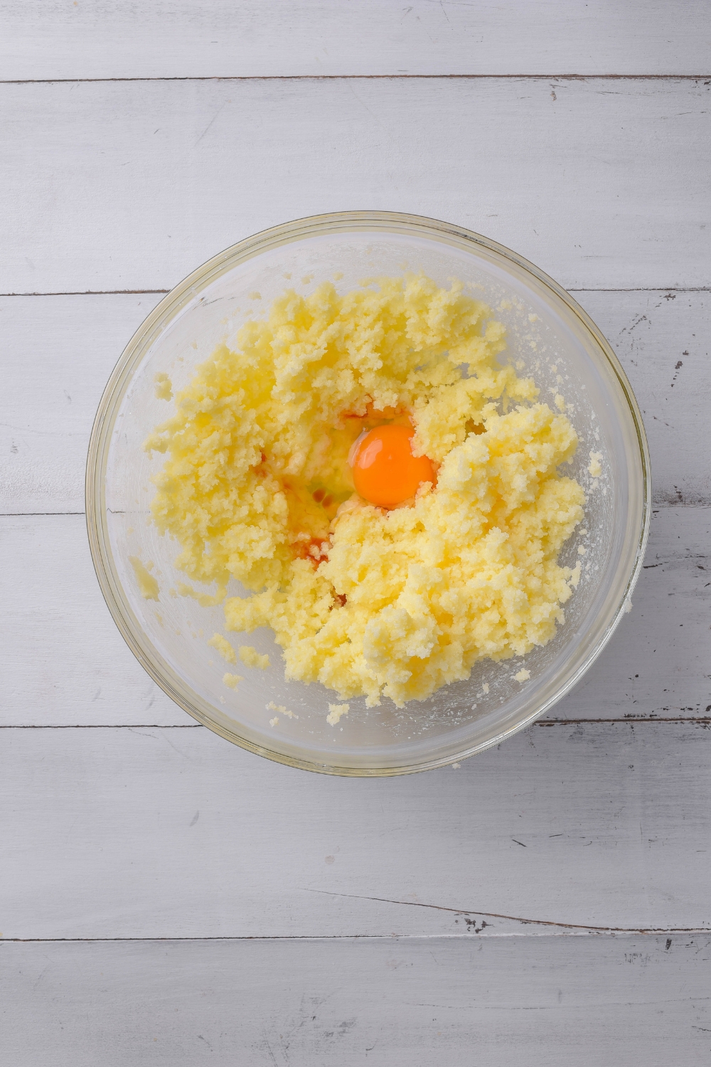 A glass bowl holds creamed butter and sugar. One egg yolk can be seen in the bowl, as well.