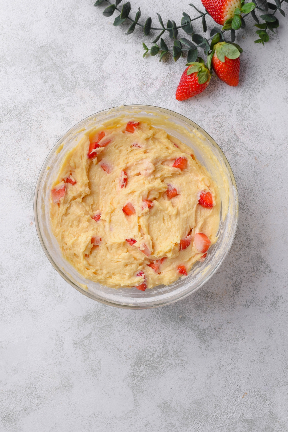 A glass bowl holds chopped strawberries and cake batter. They have been combined.