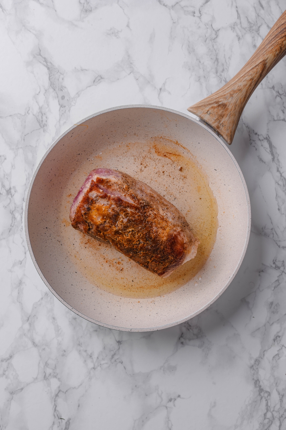 A seared venison tenderloin sits in a white frying pan.