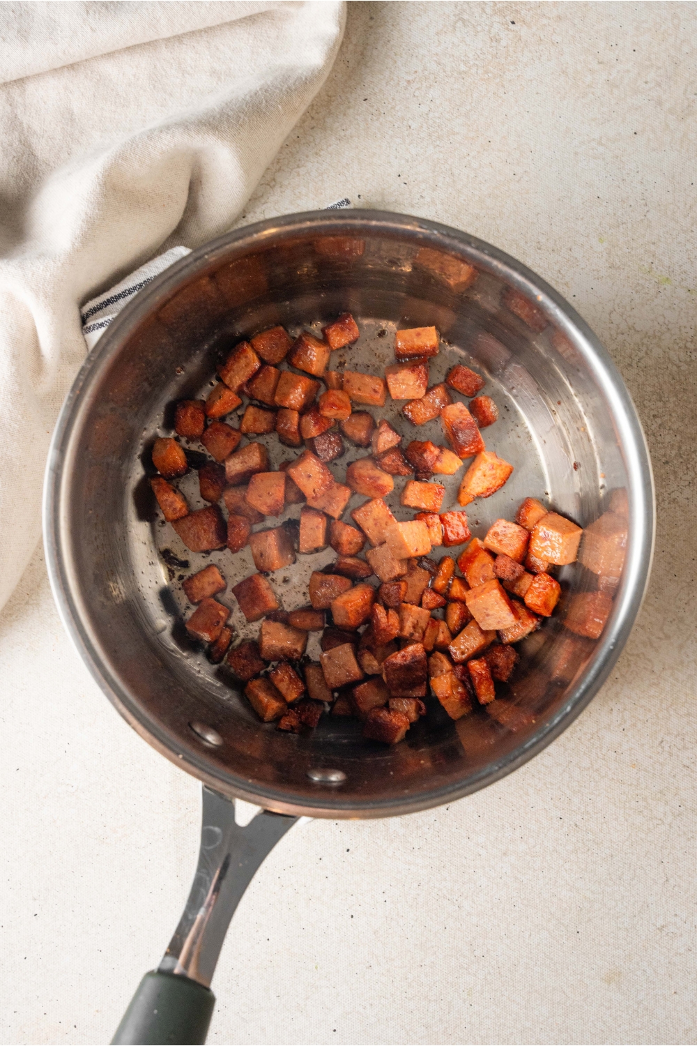 A silver sauce pan is holding caramelized pepperoni.