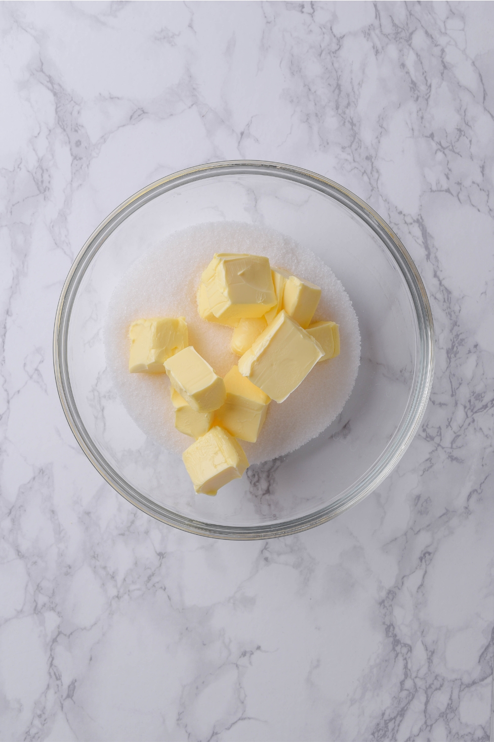 A glass bowl holds cubed butter and white granulated sugar.