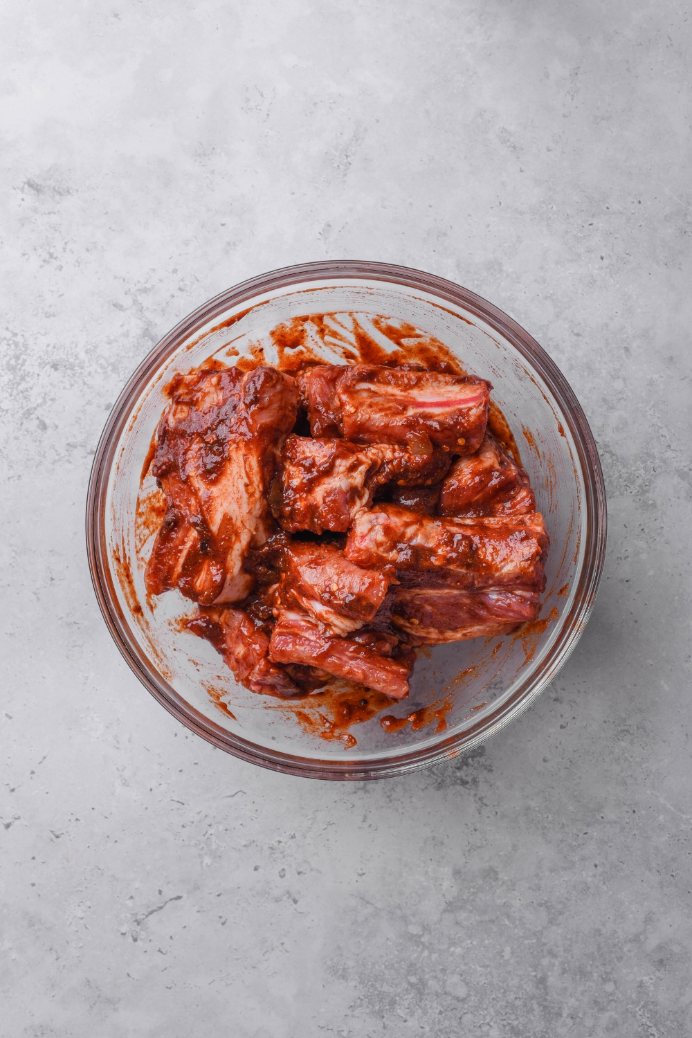 A glass bowl is full of country style ribs coated in barbecue sauce.