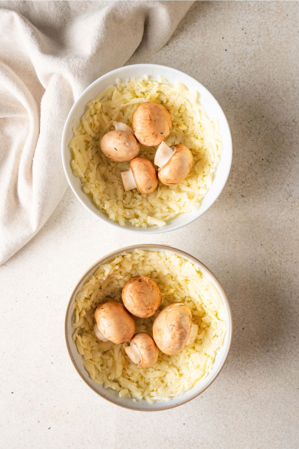 Two bowls holding mozzarella cheese and four mushrooms are on a white countertop.