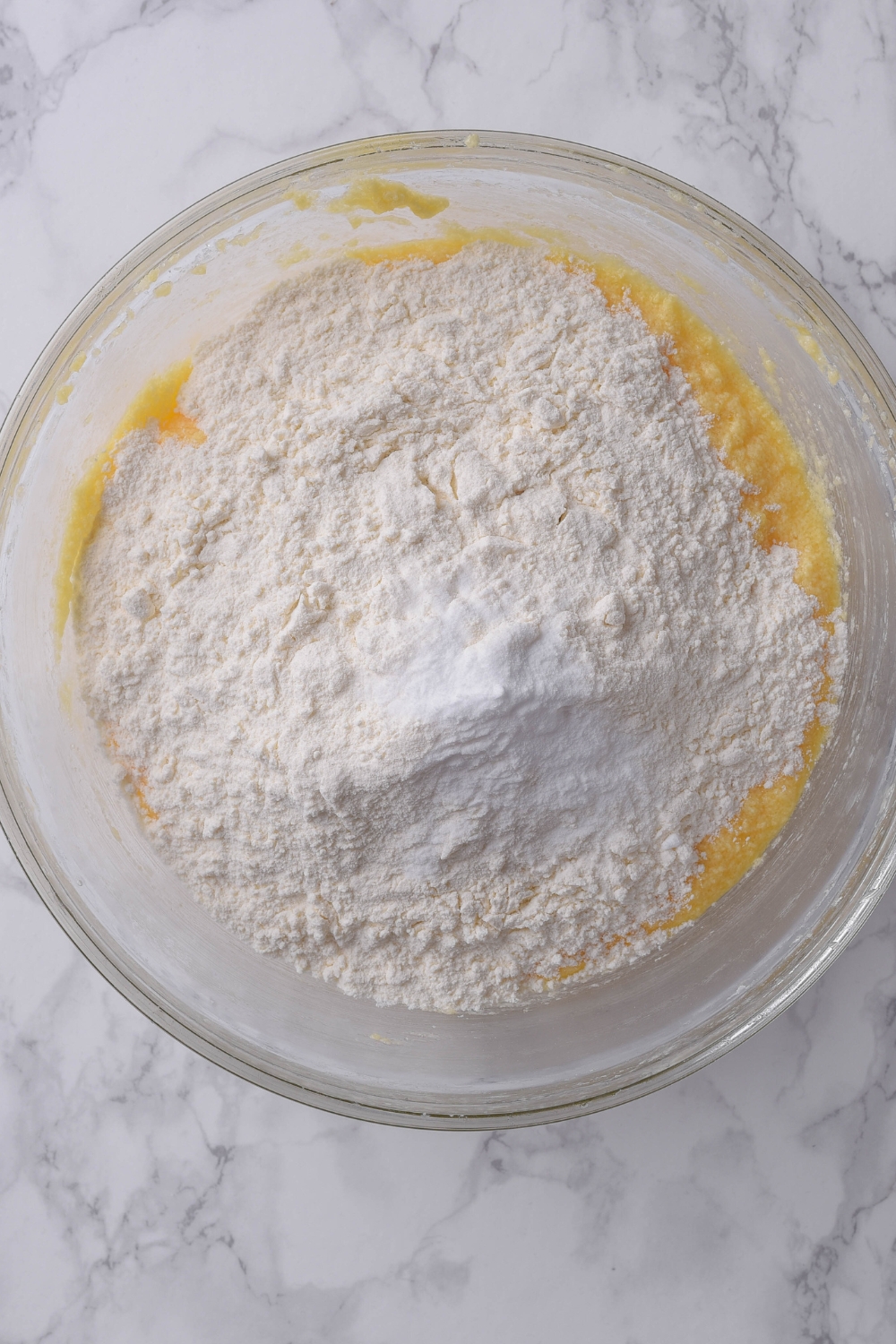 Dry ingredients sit atop creamed butter and sugar in a glass bowl waiting to be combined.