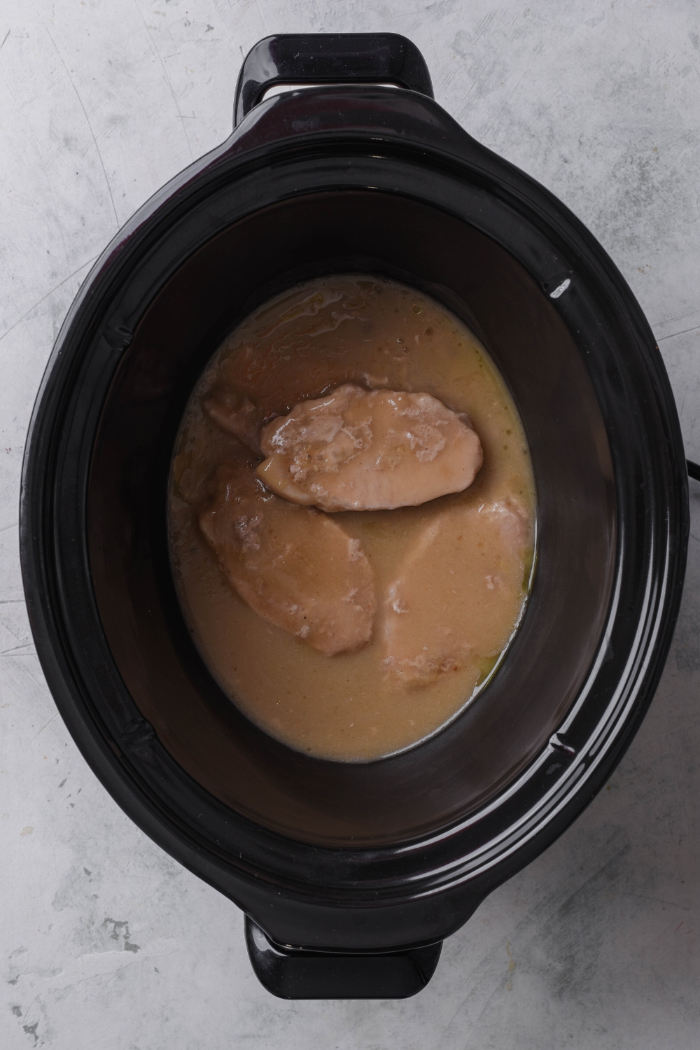 A black crock pot holds cooked pork chops with mushroom soup.