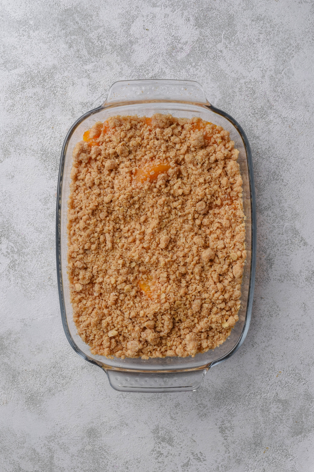 A glass baking dish holds a golden brown baked peach crisp with canned peaches.