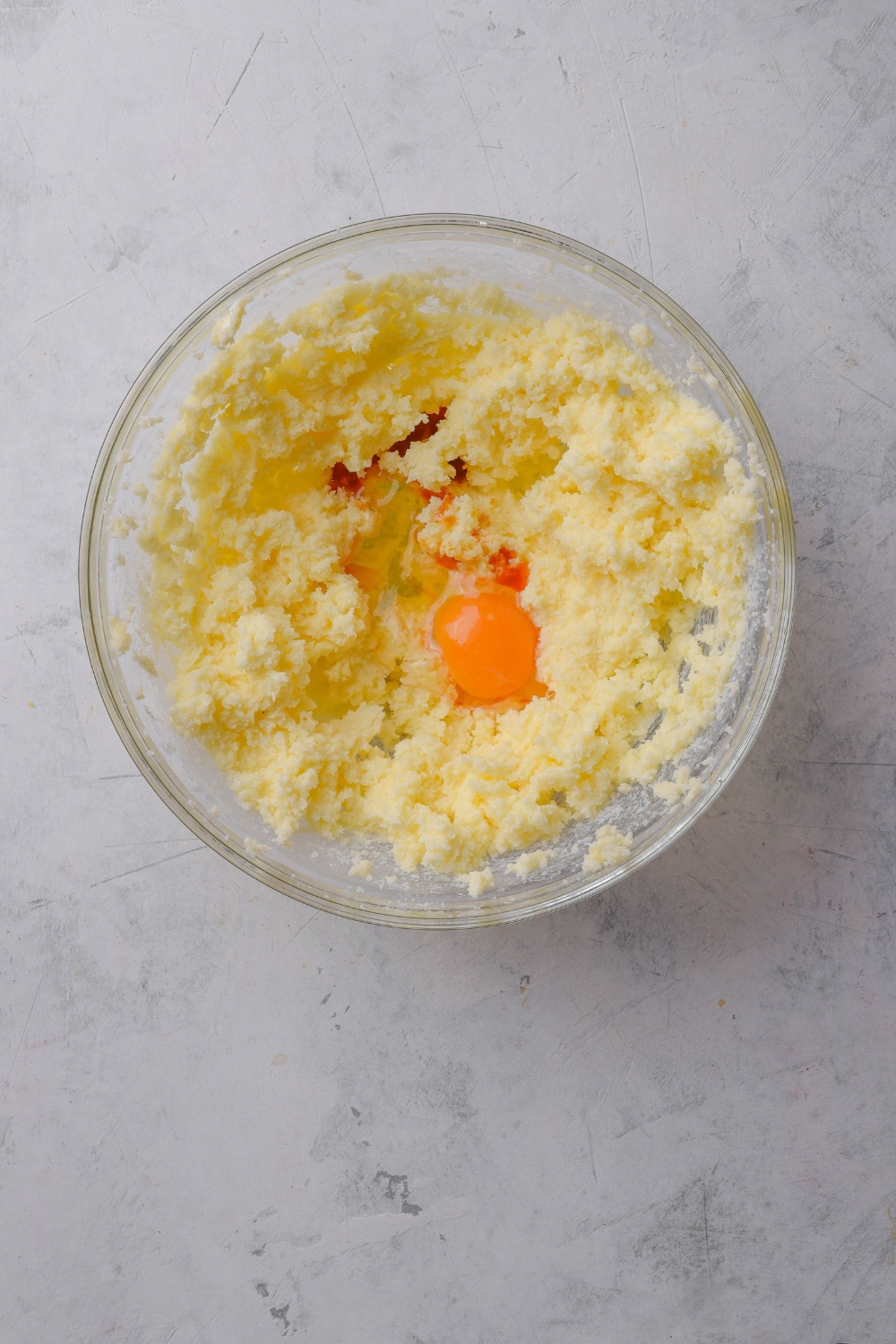 A glass bowl holds creamed butter and sugar. An egg yolk and vanilla extract are in the bowl as well.