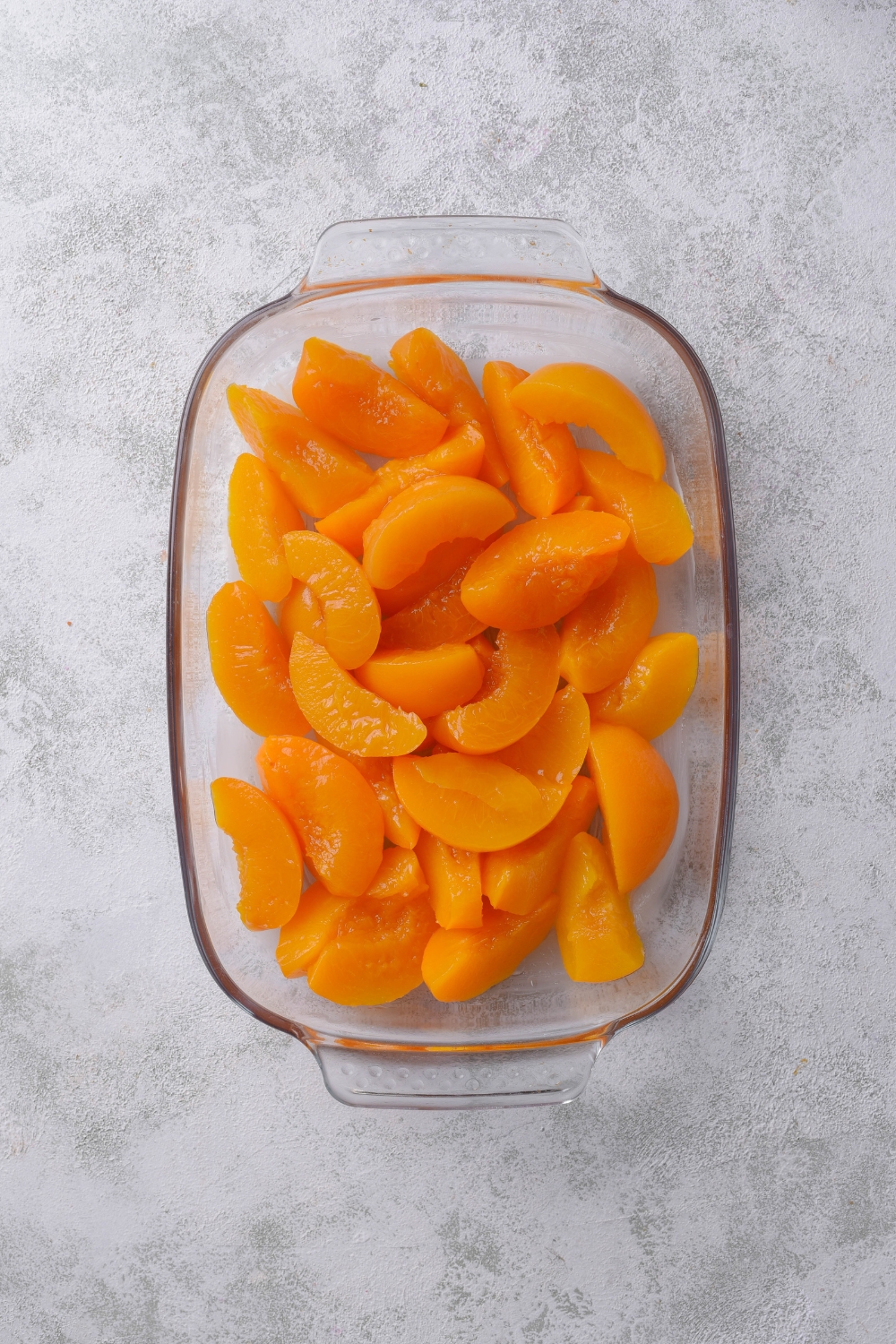 A glass baking dish holds canned peaches ready to be topped with the oat crumble.