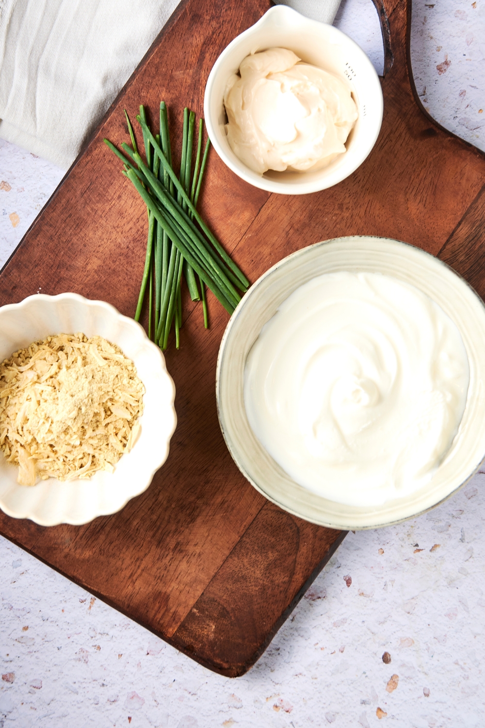 Sour cream, mayonnaise, onion soup mix, and chives are all in separate containers on a wooden serving board.