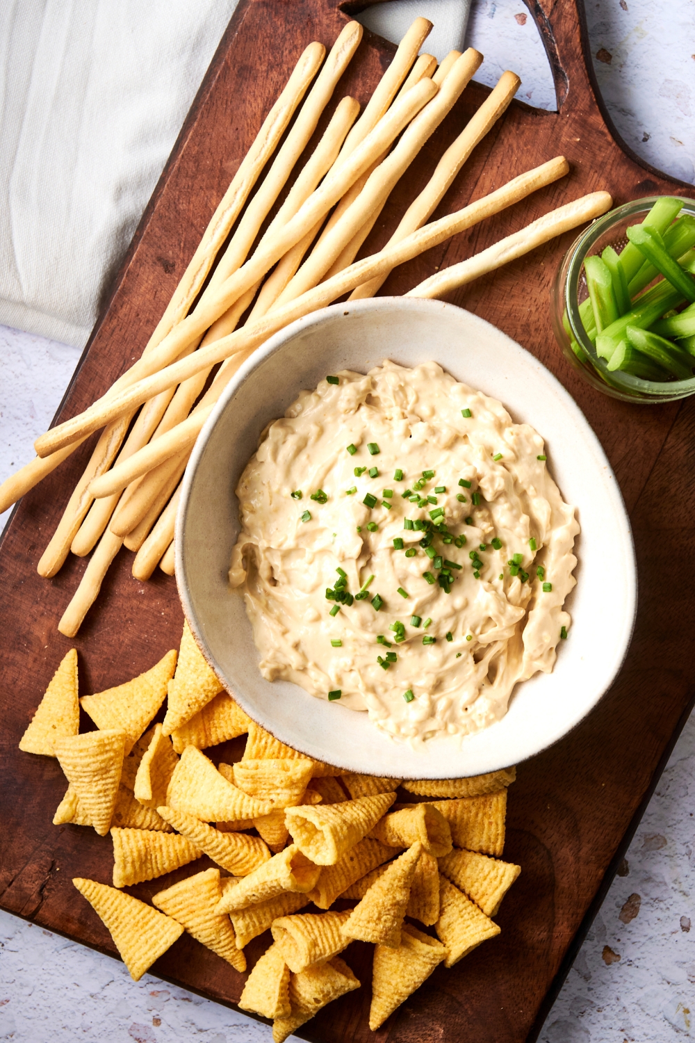A wooden serving board holds a large white bowl of Lipton french onion dip, crackers, and celery.