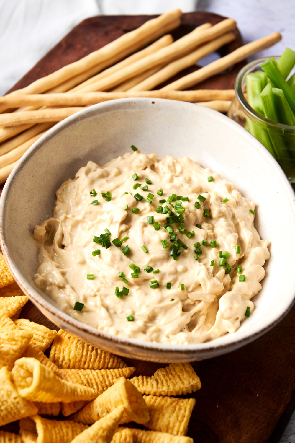 A large white bowl is full of Lipton french onion dip. The dip is garnished with chives and various crackers are nearby.