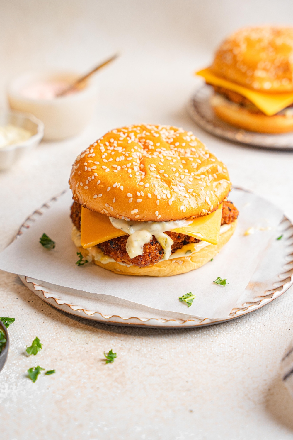 A filet o fish sandwich sits on a plate. There is another sandwich sitting behind the first sandwich.