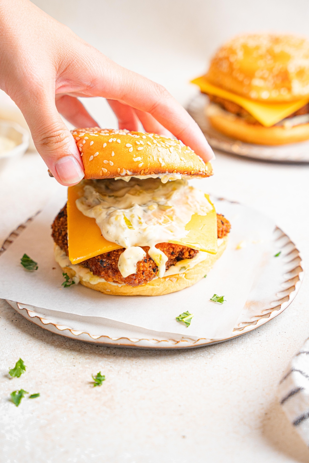 Someone adds a top bun to a filet o fish sandwich. The sandwich has garlic aioli and a slice of cheddar cheese on it.