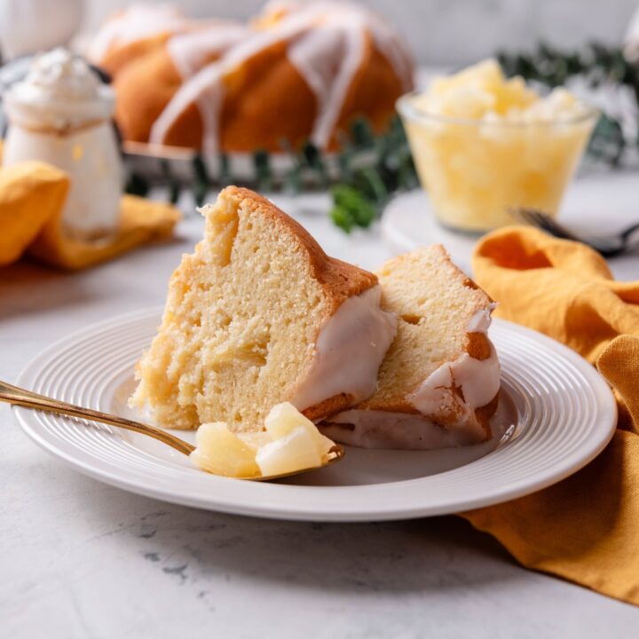 Two pieces of pineapple pound cake are on a white plate. A fork is on the plate as well.