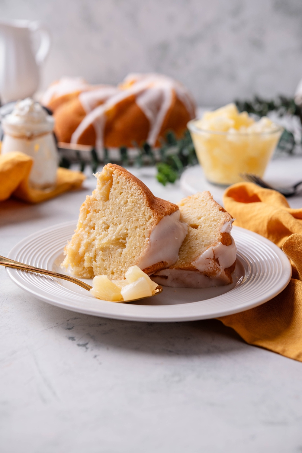 Two pieces of pineapple pound cake are on a white plate. A fork is on the plate as well.