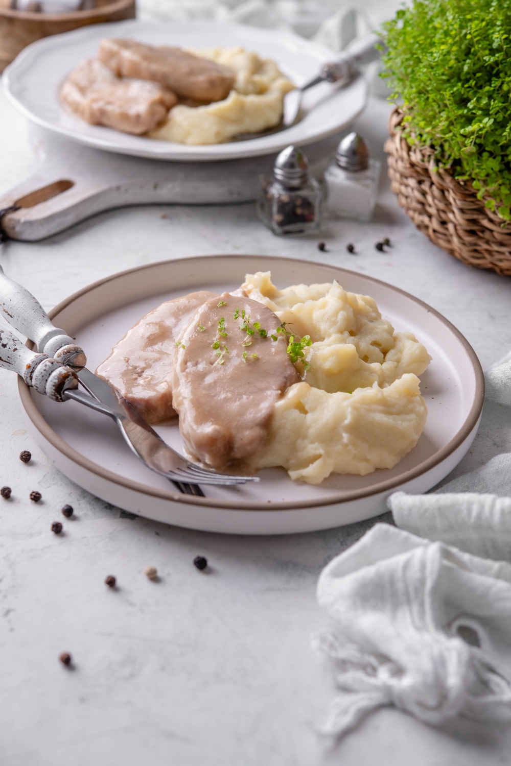 A white plate is full of pork chops and mashed potatoes. The pork chops are garnished with fresh herbs.