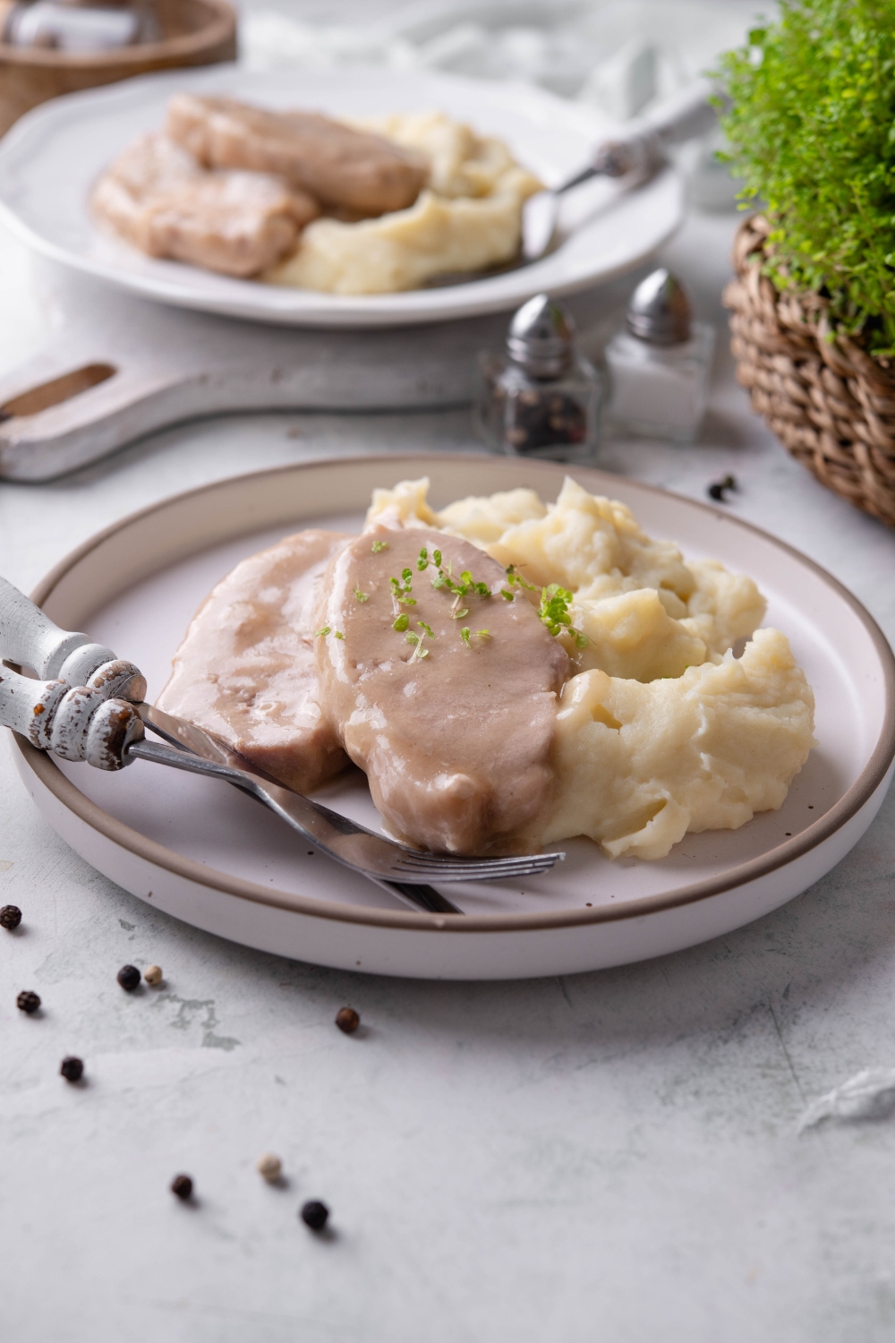 A white plate is piled high with crock pot pork chops with mushroom soup garnished with fresh herbs and mashed potatoes.