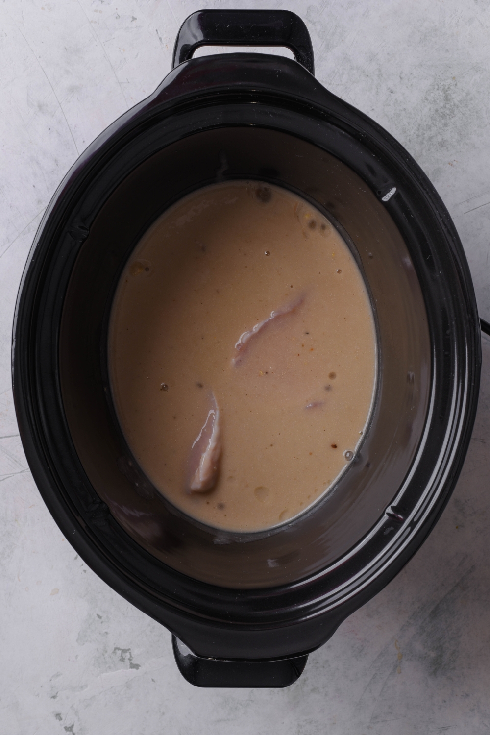 A black crock pot is full of pork chops covered in mushroom soup mix.