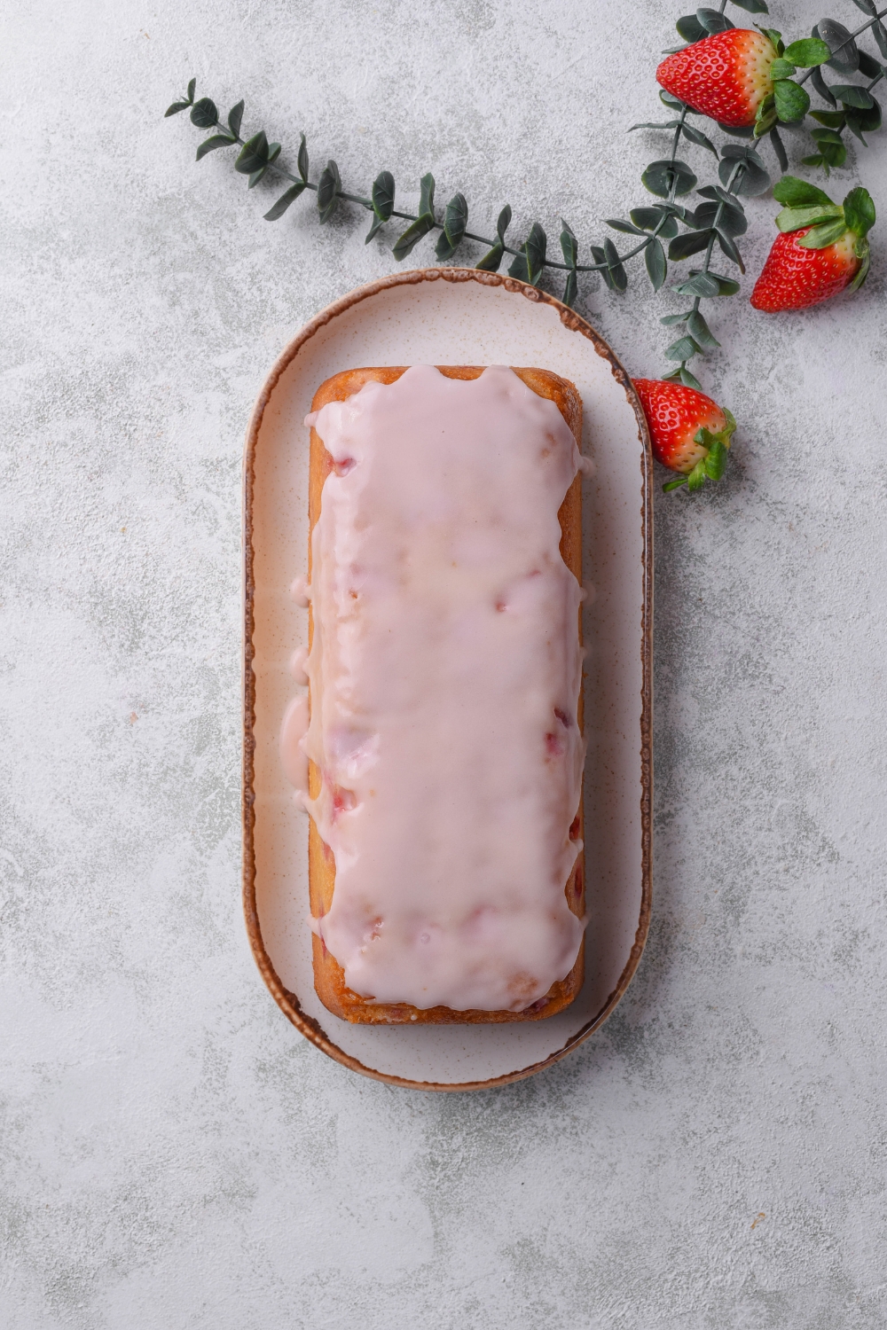 A serving platter holds a cooled strawberry pound cake. The cake has been iced with strawberry icing.