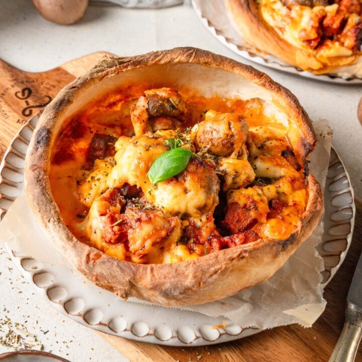 A golden brown Chicago pizza pot pie is on a white plate. There is a basil leaf garnishing the pot pie.