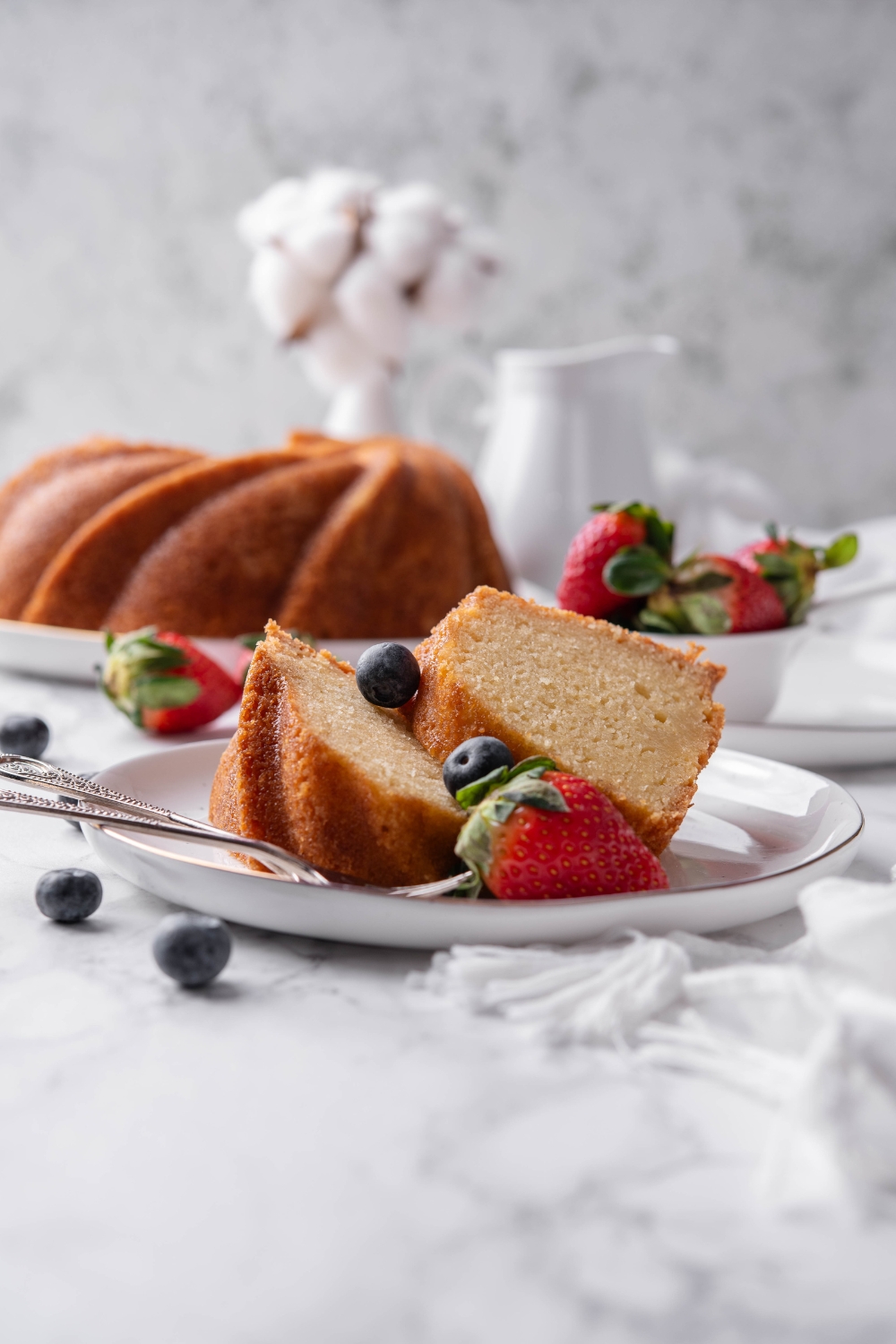 Two slices of buttermilk pound cake are on a white plate. Berries and forks are on the plate as well.