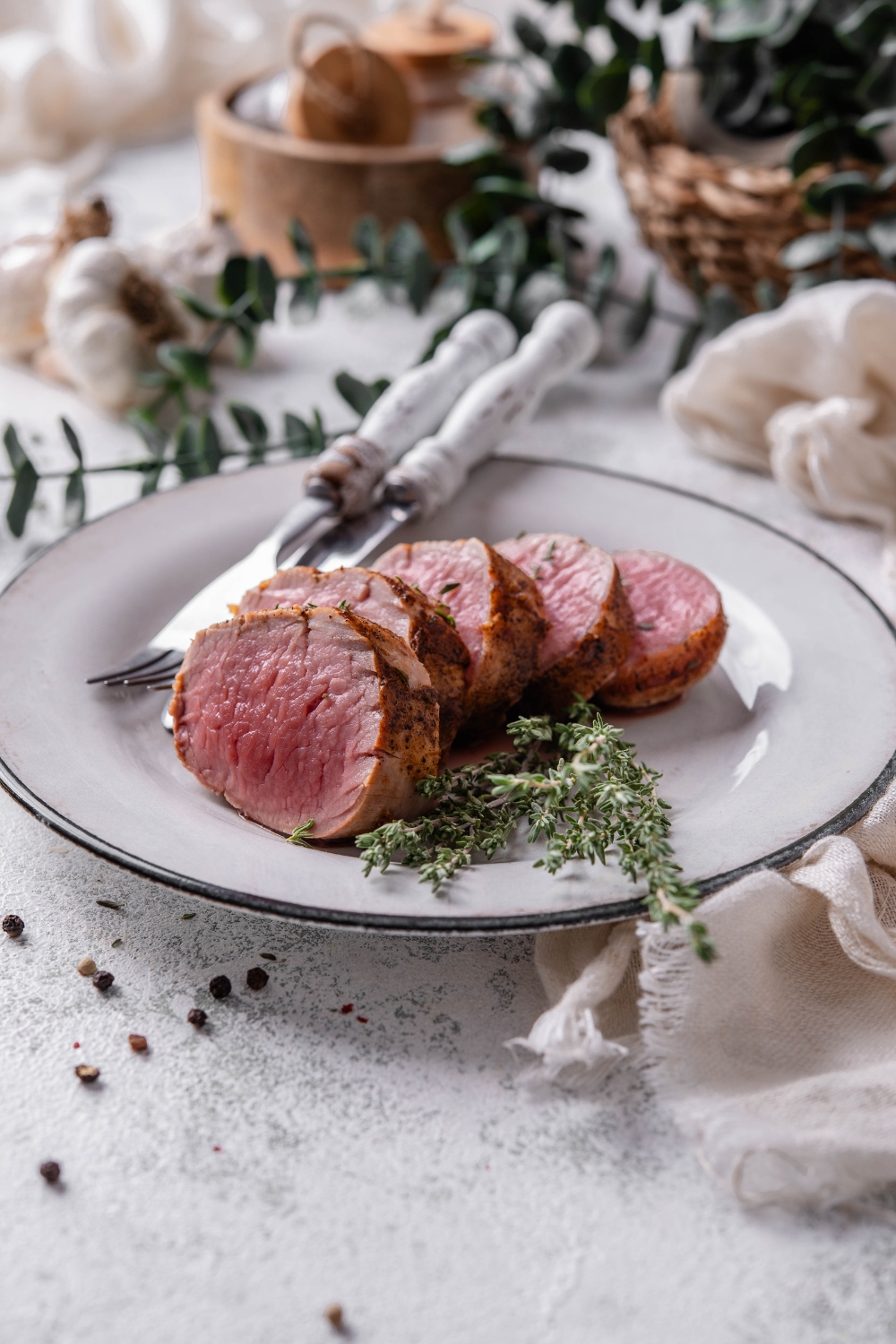 A white plate holds a sliced venison tenderloin. A sprig of fresh herbs is on the plate as well.