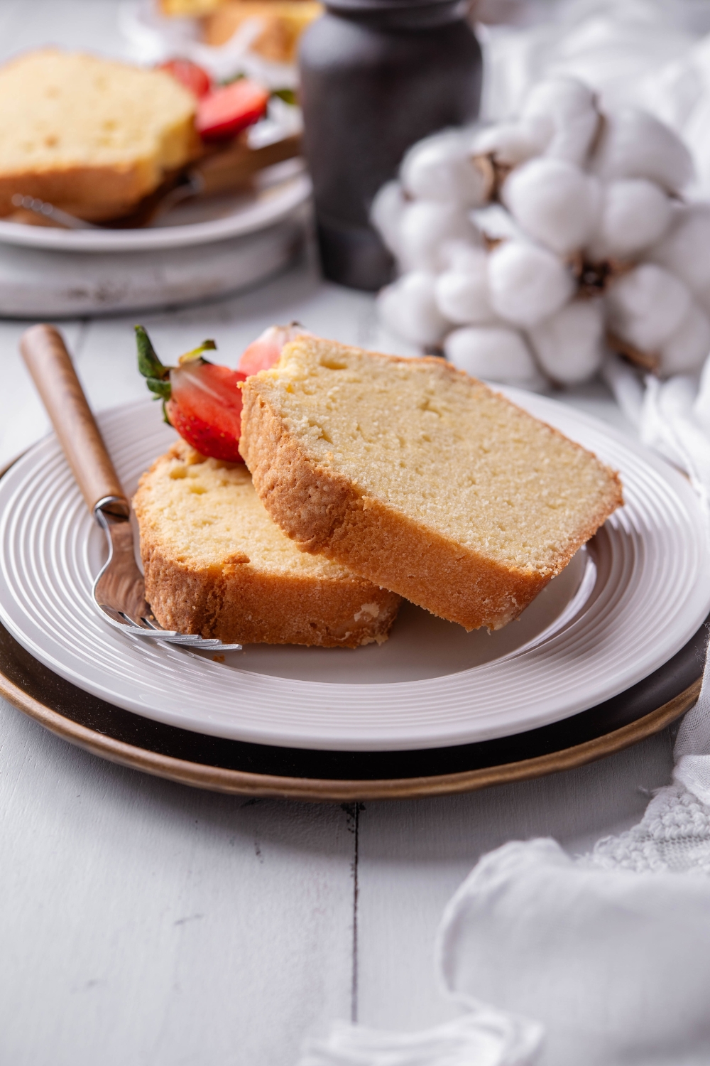 A white plate holds two thick slices of old fashioned pound cake. A fork and strawberries are on the plate.