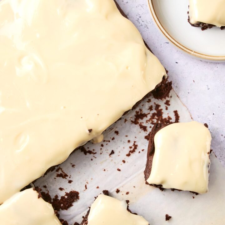 Parchment paper with brownies with cream cheese frosting. Some are cut into squares and the remaining brownies are on the parchment paper.