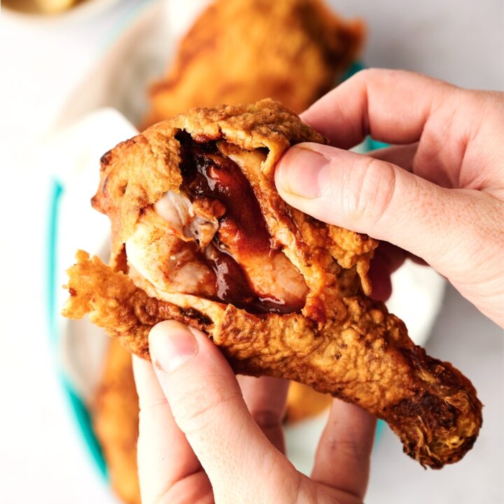 A hand pulling apart a piece o fried chicken showing the inside with a sauce.