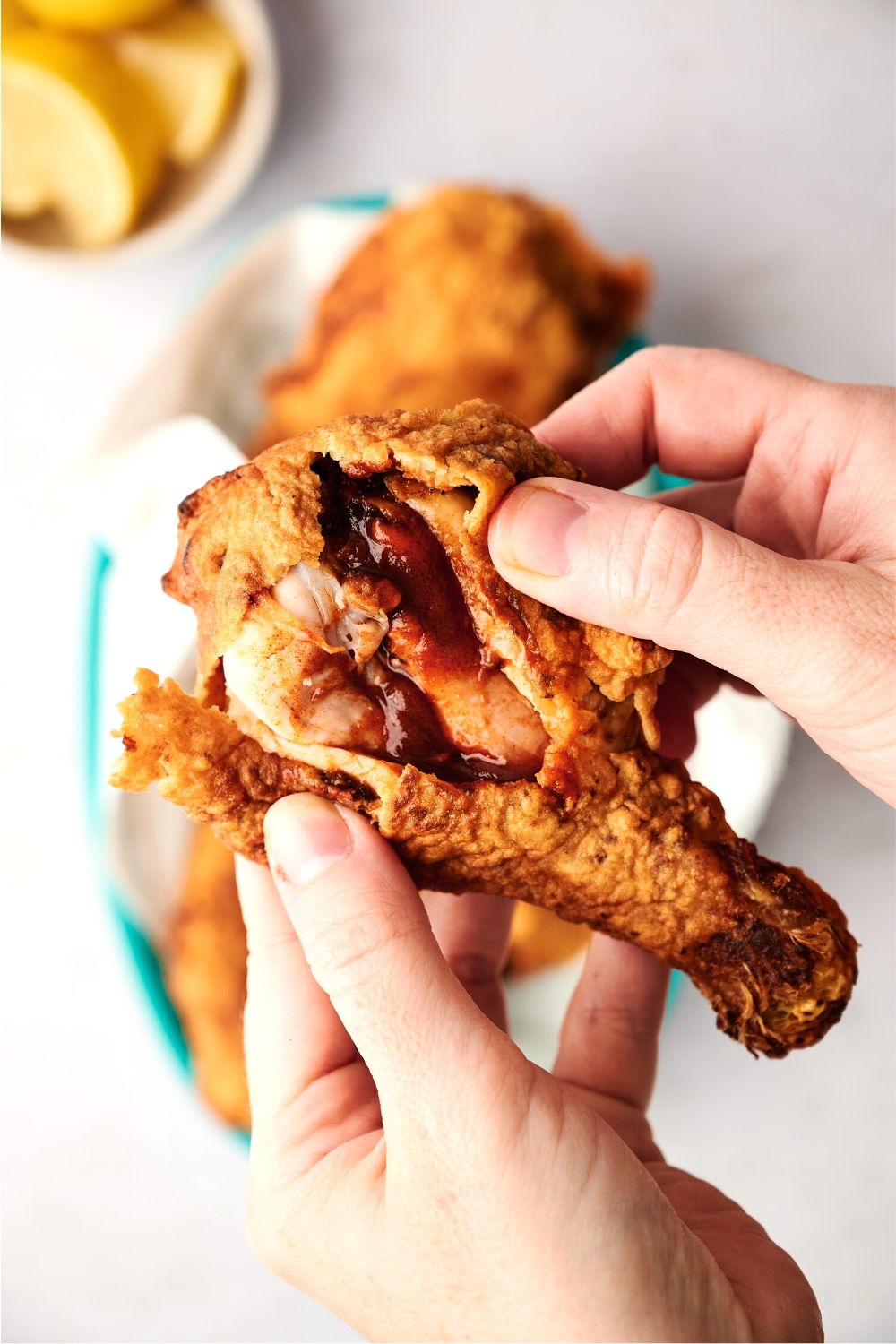 A hand pulling apart a piece o fried chicken showing the inside with a sauce.